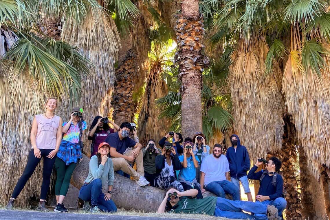 a group of students pose in front of palm trees