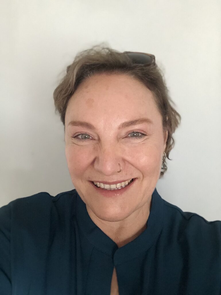 a woman with short, dark blond hair wearing a black shirt smiles at the camera